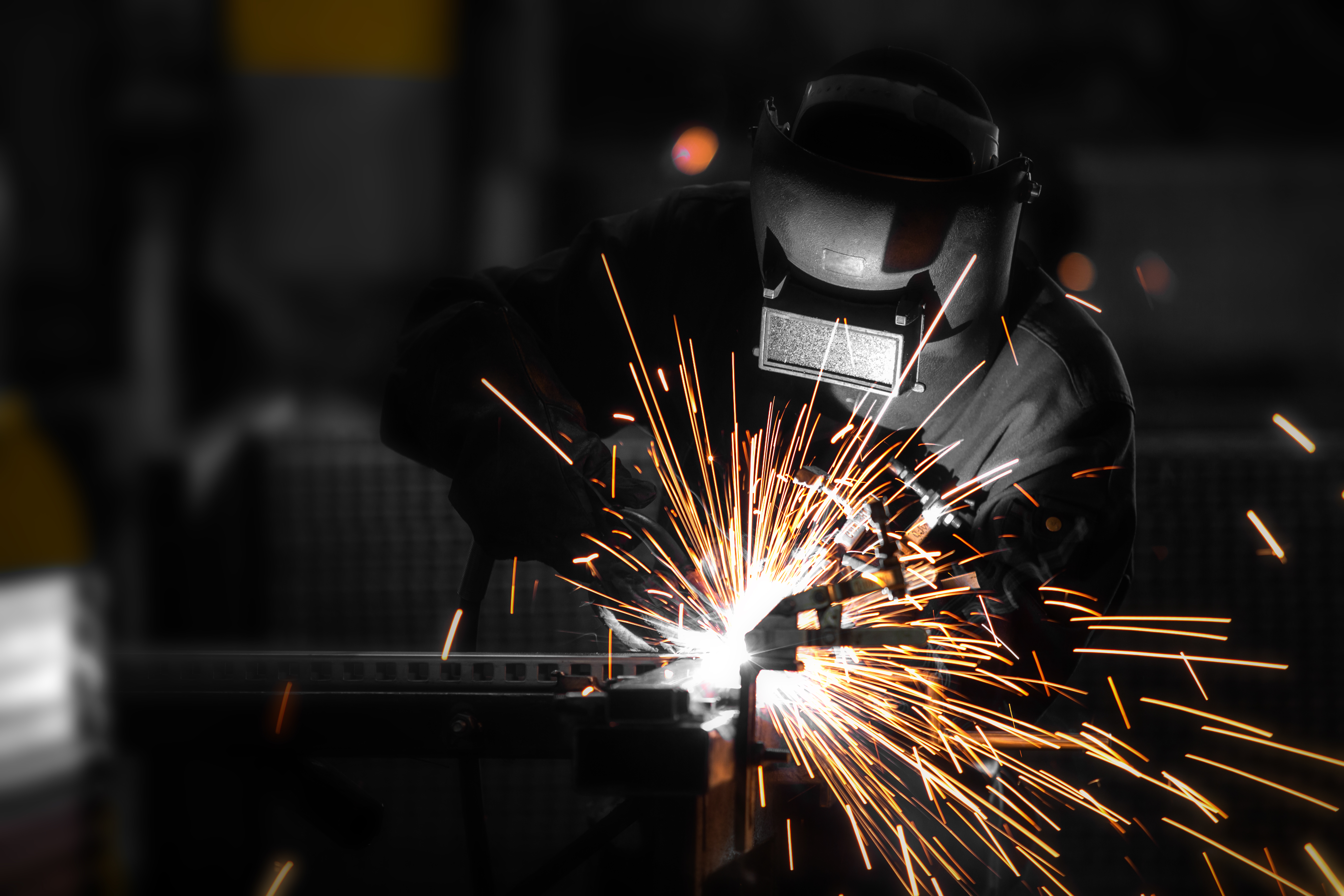 A welder is cutting through steel, set in a dark backgound with bright sparks flying.